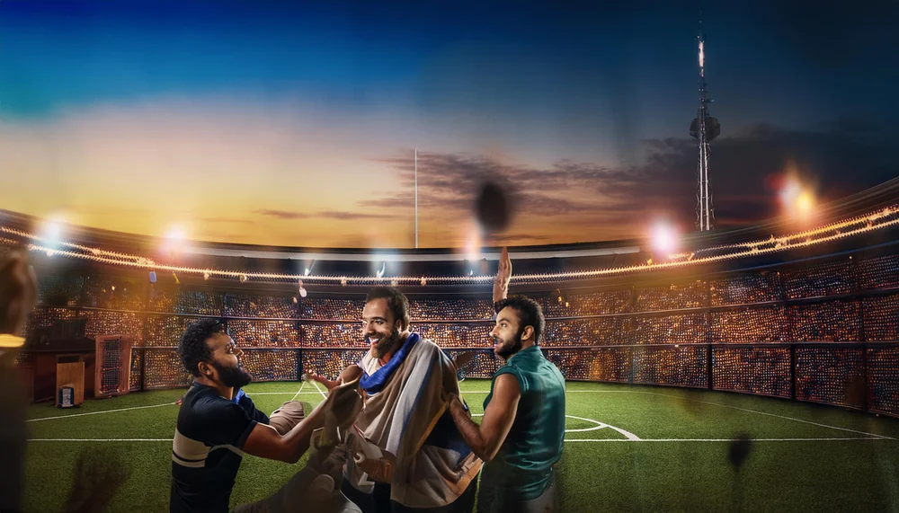 Three friends celebrating a wicket inside a floodlit cricket stadium at dusk